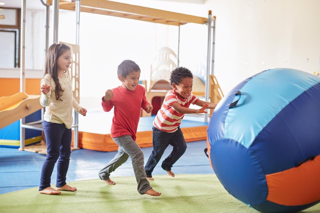 Children running toward a large play ball at Gymboree